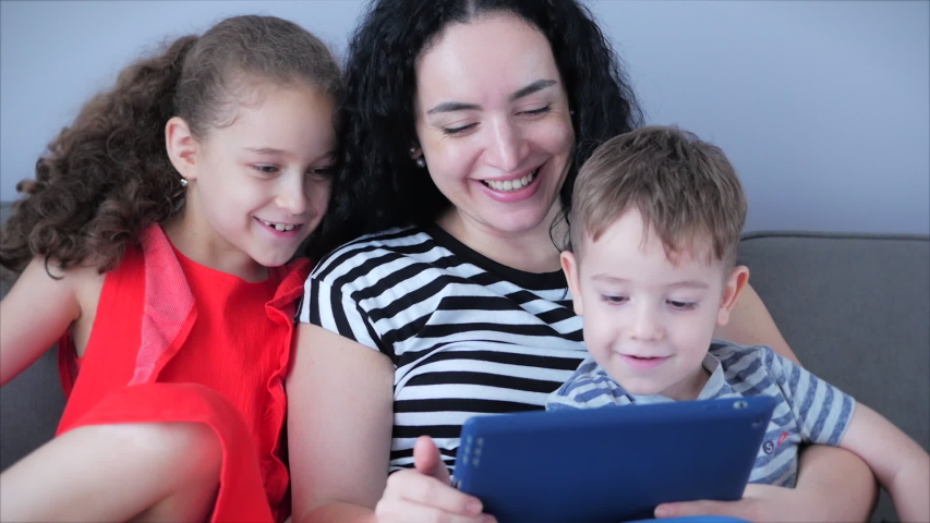 Happy family,mom and cute little children watch the phone,mom plays with children at home,relaxing using a smartphone,hugging,sitting on the couch, laughing, having fun,enjoying moments of family life
