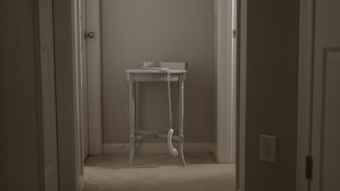 Retro 80s and 90s corded telephone dangling off the hook in dark mysterious home hallway.