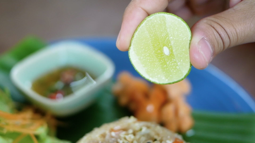 Close up hand of Woman squeezing limes on pork fried rice ready to eat. Thai style cuisine.
