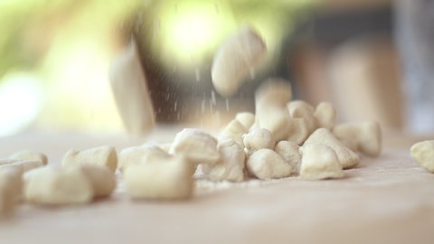 Woman making homemade pasta potato gnocchi. Dropping the dough pieces onto the floured wooden table.