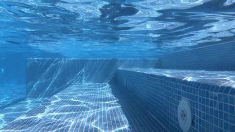 SLOW M - Bottom of the swimming pool. Clear water background with the reflection of sun rays underwater. Amazing view from underwater camera. Inflowing water jet into a swimming pool with blue tiles. 