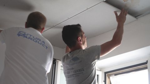 Modugno, Italy - 14 July 2020: two workers mount a plasterboard false ceiling by screwing them to a metal support structure