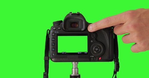 Photographer's male hand is pressing a record button. DSLR camera isolated on keyed green screen recording video. Professional digital camera standing on tripod. Closeup LCD monitor. Shooting Process.