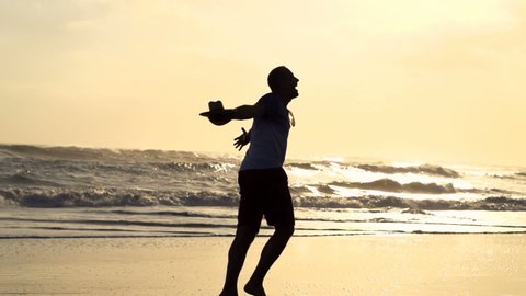 Silhouette of happy man running on beach during sunset