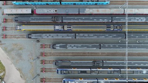 Aerial top down view of railway hub several trains parked next to each other showing the dark grey roofs and colorful train sides in between the permanent way 4k high resolution quality footage