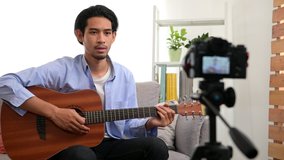 Smart young professional Asian guitar player use digital camera recording online guitar course lesson for learning from home online platform during coronavirus pandemic. Technology education concept.