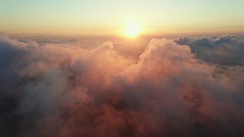 Moving white clouds blue sky scenic aerial view sunrise. Drone flies high back in blue sky through fluffy clouds in morning at orange sun summer. Sun is hidden behind clouds at fog. Relax. Nature