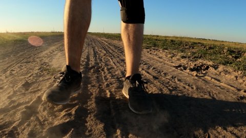 Man running on dusty dirt road through countryside, close up of legs in slow motion