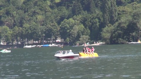 Banana Boat with some tourists making a joyride along a beautiful lake in the alps.  Zell am See, Kaprun, Salzburg, Austria. Tubing jaunt banana ship stunt on the water.