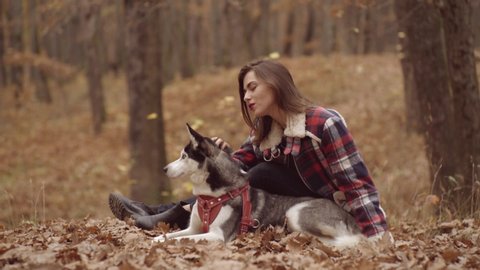 Autumn fashion trend. Young beautiful woman with husky dog walking in park. Alaskan Malamute on nature in the autumn park
