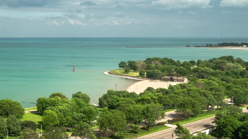 Zoom out time lapse as traffic speeds by on Lake Shore Drive in Chicago as fluffy white clouds float by overhead as they head towards the blue water of Lake Michigan.