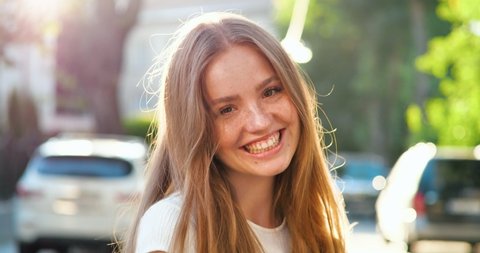 Portrait of Gorgeous young Woman with Golden Red hair is smiling Charmingly at the Camera. An attractive young Woman is walking down the Streets, turns to Camera, showing sincerely Emotions.