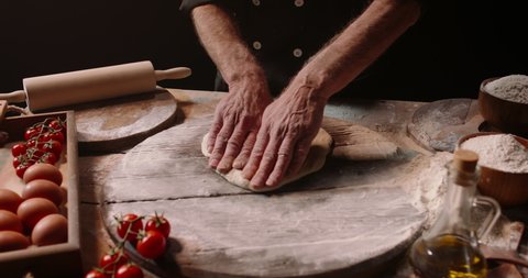 Senior professional italian restaurant chef working, shaping floured dough for pizza. Experienced cooker making pizza using traditional recipe, isolated on black background close up 4k footage