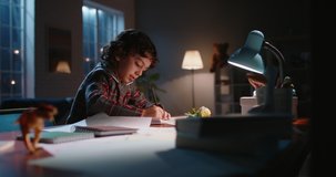 Funny little asian kid drawing at home. Boy with curly hair drawing with pencils on paper in the evening, learning art, having fun at home - hobby concept 4k footage