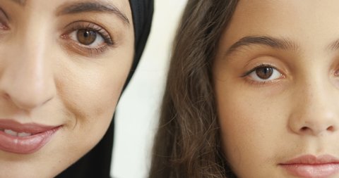 Close up of half faces of young beautiful Arab woman in black hijab and pretty little girl. White background. Portrait. Smiled happy muslim mother in headcarf and charming small daughter.