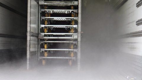 Ice cold mist blowing from freezer of refrigerated trailer of truck. Transporting food and drink both frozen and chilled. Technology used by food produce industry. Stacked steel metal trolley wheels.