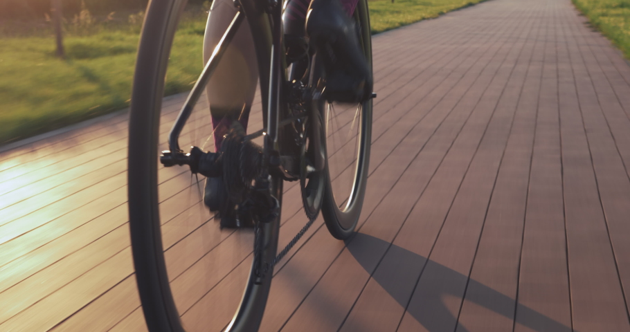 Bike wheel rotation in sunset light. Woman is pedaling bike at sunrise, close up of bike gear. Cyclist twists pedals on bicycle on cycle path at sunset. Cycling gear, chain and cassette. Sport concept Royalty-Free Stock Footage #1056982706