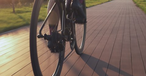 Bike wheel rotation in sunset light. Woman is pedaling bike at sunrise, close up of bike gear. Cyclist twists pedals on bicycle on cycle path at sunset. Cycling gear, chain and cassette. Sport concept