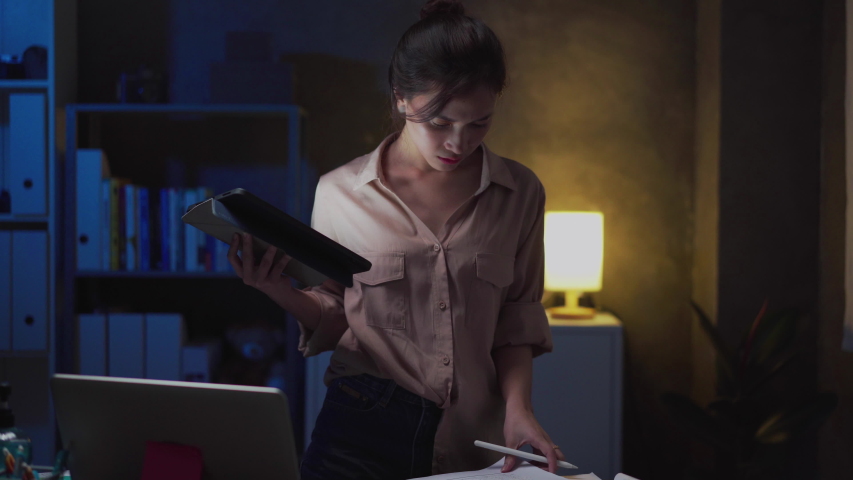 Asian woman remote working late at home while coronavirus pandemic. Ms or medium shot of young Asian woman working late at home. Work from home life,domestic lifestyle, self isolation or quarantine. Royalty-Free Stock Footage #1056984281