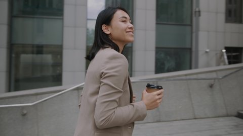 Young rich successful businesswoman walks upstairs with coffee to enter office building working in beautiful modern business center.