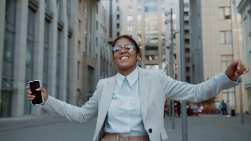 Happy excited businesswoman young entrepreneur celebrating victory dancing with smartphone on street having fun enjoy job opportunities. Career people. Celebration. | Shutterstock HD Video #1056986498