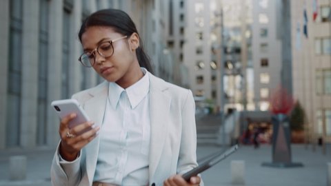 Young Ambitious mixed-race latin businesswoman using cellphone for internet connection messaging in the street. Business person. Technologies. Modern people.