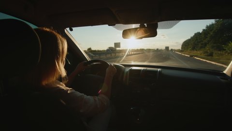 Woman driver behind the wheel of a car drives on the highway at sunset