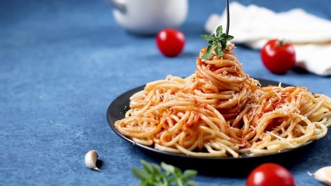 Screw traditional Italian spaghetti bolognese onto a fork on a black round plate on a blue background. Ingredients for the pasta are cherry tomatoes, parmesan, garlic, olive oil, basil.