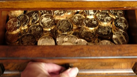Female hand closing an old wooden drawer full of bullion gold coins.