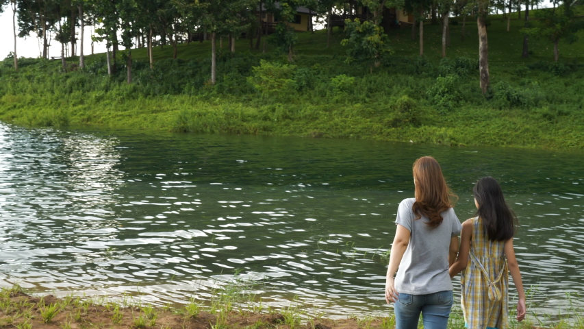 4k happy asian girl walking with her mother in the field beside the lake