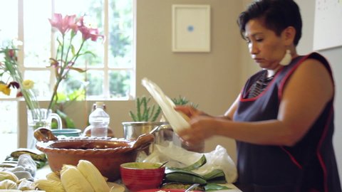 Mexican woman making authentic steamed Tamales with mole negro and Salsa verde in a humble kitchen and livingroom with olla de barro and banana leaves. With corn dough mixed with her own hands.
