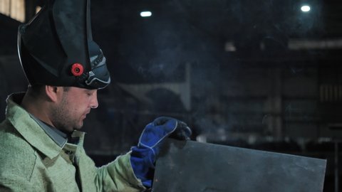 Professional Welder Wearing Safety Uniform Puts on Mask, Starts Assembly, Gets to Heat Soldering Work at Heavy Manufacturing Factory Closeup Indoor. Metalwork Welding, Job Process of Industrial Worker