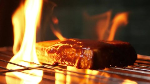 Closeup of a cottage cheese steak being barbecued on a grill with dramatic smoke and fire