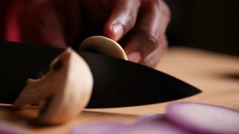 Slow motion closeup sliding or truck shot of a mushroom being chopped with a black chef knife on a cutting board
