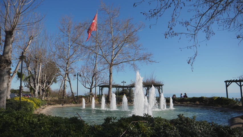 Establishing shot, fountain park in Antalya trees and turkey flag, people walking around in the background.