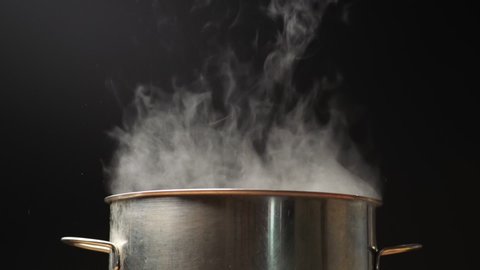 Pot and steam in the kitchen. Steam comes out of the pan while cooking. Boiling water in pan on black background. Slow motion shot