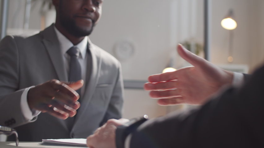 Close up shot of African American businessman giving a handshake to a Caucasian colleague and speaking with him while sitting at the office table. Royalty-Free Stock Footage #1057012802