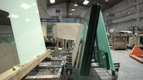 Warehouse of glass panels. Glass sheets stacked one on another on a glass holding cart in the industry workshop. Orange manual forklift in the background.