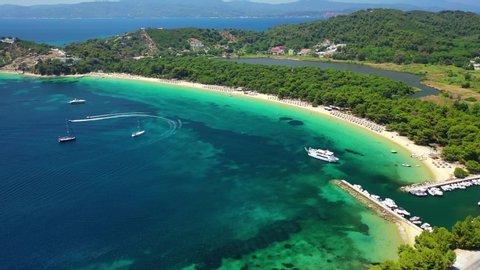 Aerial drone video of beautiful popular organised sandy bay, turquoise beach and natural preserve lake with pine trees of Koukounaries, Skiathos island, Sporades, Greece