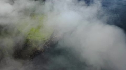 Rugged Faroe Islands coastline aerial reveal through sea clouds, high cinematic