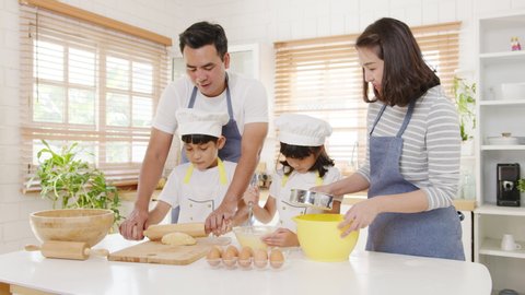 Happy smiling young Asian Japanese family with preschool kids have fun cooking baking pastry or pie for breakfast meal in modern kitchen home in the morning. Doing bakery knead dough and bake cookies.