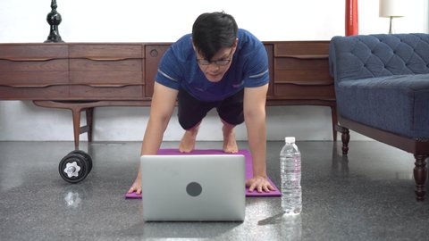 young asian fit man in sportswear doing plank While watching video training fitness  online tutorials on laptop in living room at home . sport male workout in quarantine