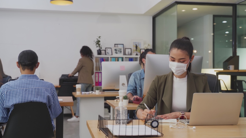 Group of Asian team business people working in office with new normal lifestyle concept. Man and woman wear protective face mask and keep distancing to prevent covid virus in company workplace. Royalty-Free Stock Footage #1057039688