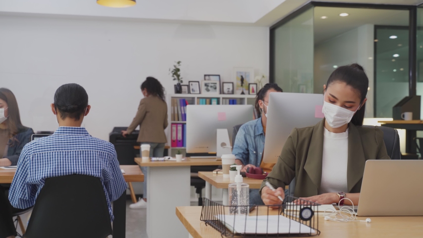 Group of Asian team business people working in office with new normal lifestyle concept. Man and woman wear protective face mask and keep distancing to prevent covid virus in company workplace. Royalty-Free Stock Footage #1057039688
