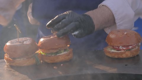 Chef hands preparing burgers on black brazier at summer local food festival - close up view. Outdoor cooking, cookery, gastronomy and street food concept
