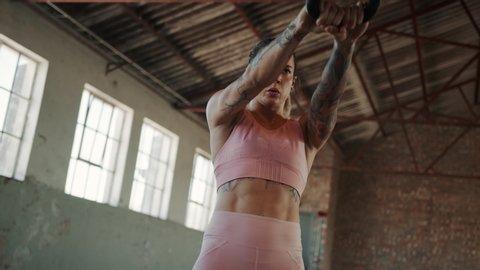Fitness woman working out with kettle bell inside abandoned warehouse. Female with muscular body exercise with kettlebell at cross training gym.
