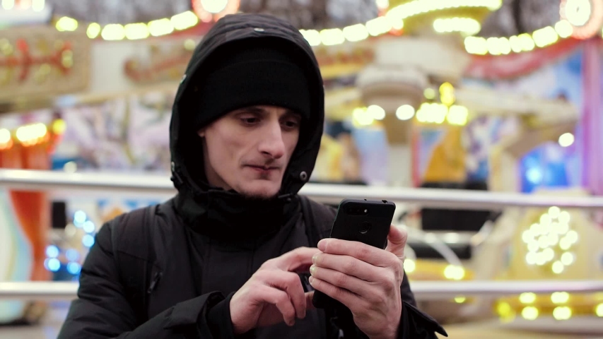 Young handsome man in black jacket and cap having video call on smartphone, slow motion