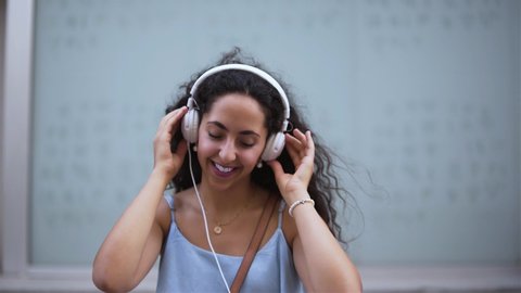 Happy hipster woman using mobile phone, listening to music online and dancing in city