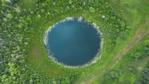 Aerial top down hyperlapse amazing lake of round shape. Cloudy sky reflected in clear turquoise water of pond surrounded by trees and plants. Ripple on water surface, windy sunny summer day