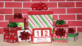 HD Video countdown to Christmas with  white wood blocks in a red box with presents stacked around it on light wood floor, cartoonish red brick background. 12 days counting down to bubbles falling xmas